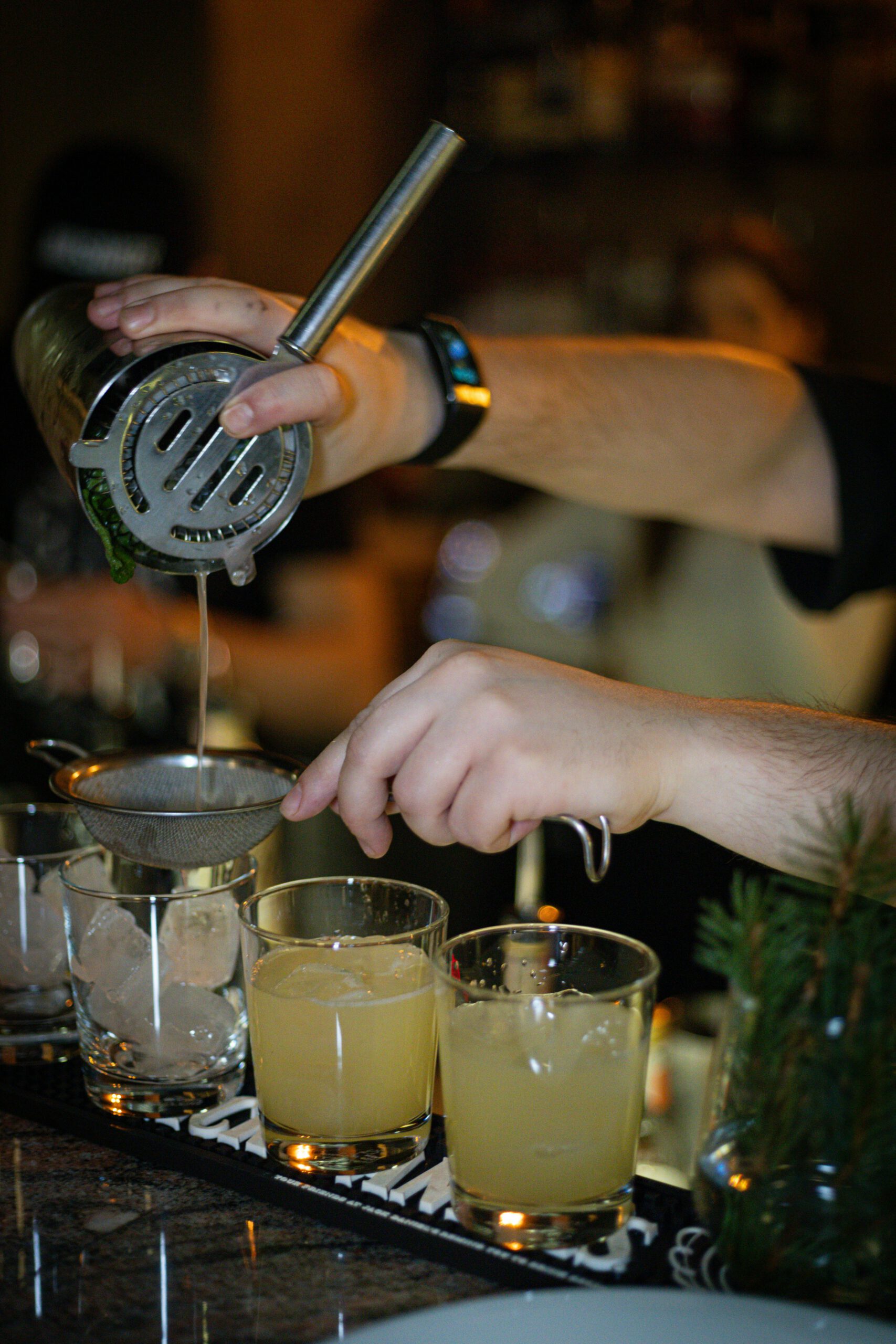 Bartender mixing citrus cocktails with a strainer at an indoor bar.
