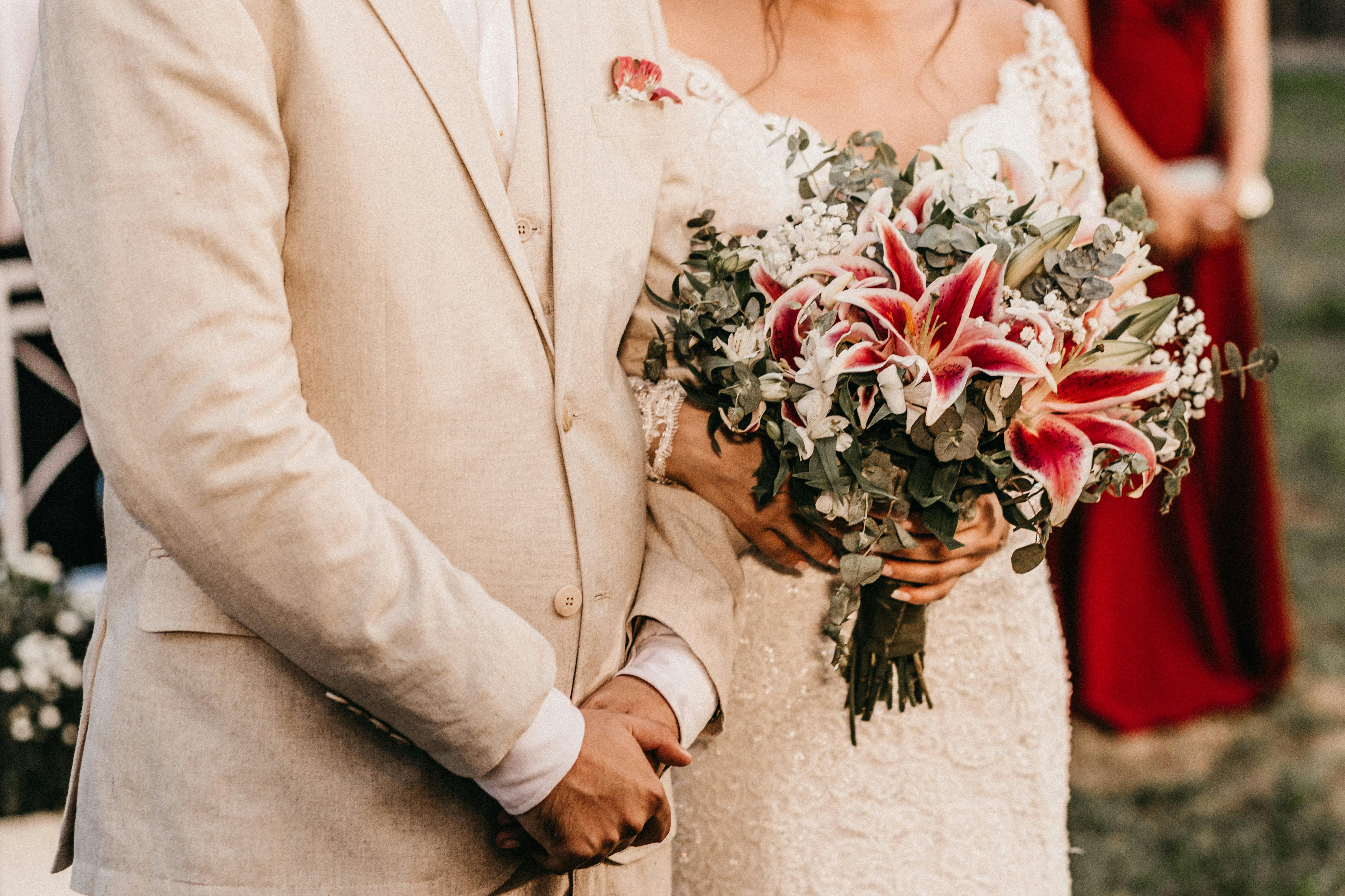 A close-up of a bride and groom holding a stunning floral bouquet on their wedding day.